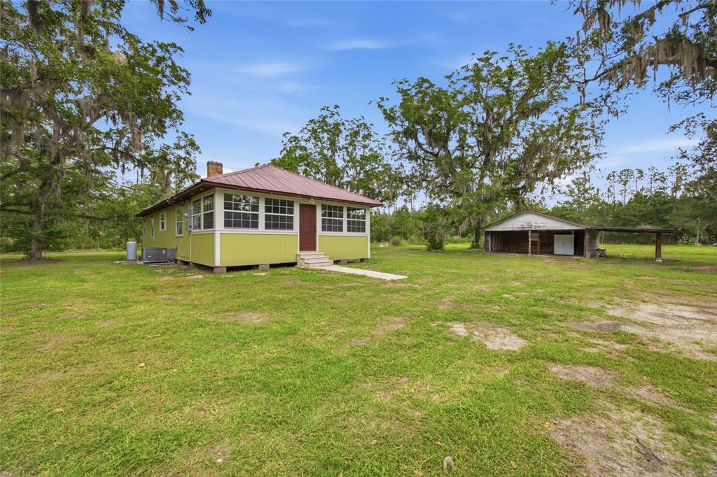 A yellow house with a metal roof and a detached shed sit on a lawn — 13216 NE 140TH STREET, WALDO, FL
