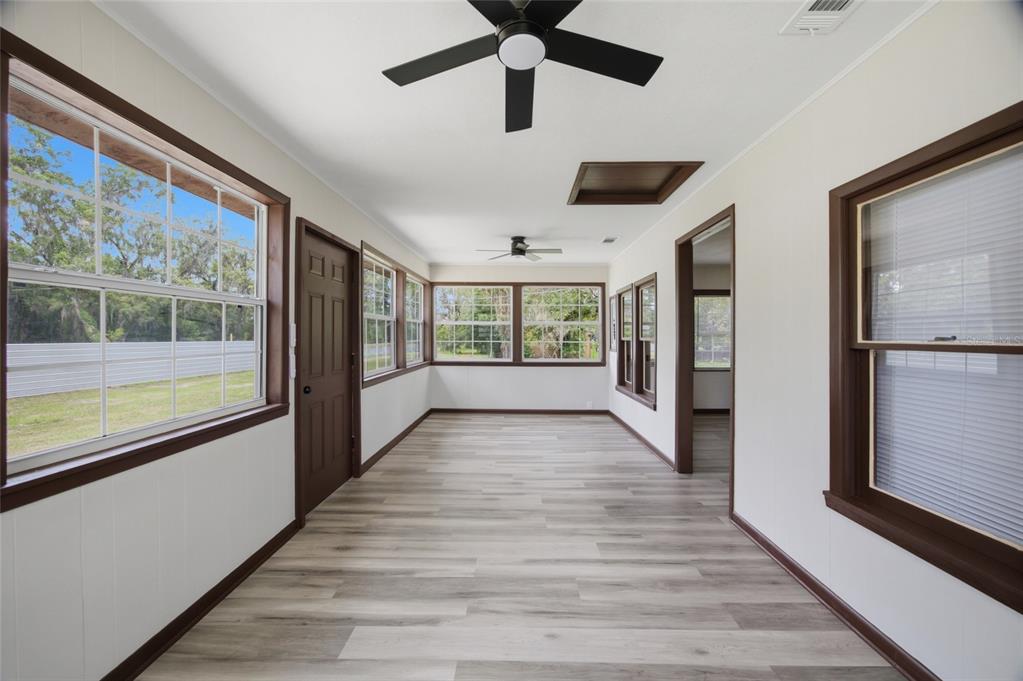 A sunroom features light wood-look flooring, white walls, dark trim, and two ceiling fans — 13216 NE 140TH STREET, WALDO, FL