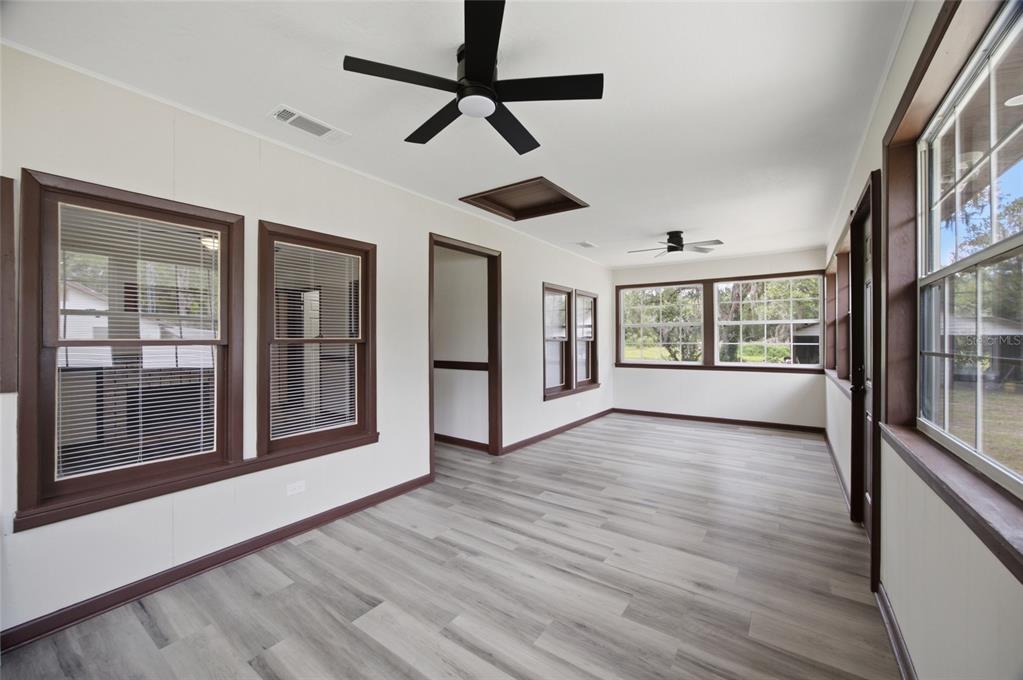 A sunroom with light wood-look flooring, white walls, dark window trim, and two ceiling fans — 13216 NE 140TH STREET, WALDO, FL