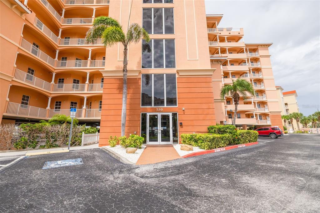 A multi-story peach-colored apartment building features a glass entrance, balconies, and a palm tree — 530 S GULFVIEW BOULEVARD UNIT 205, CLEARWATER, FL
