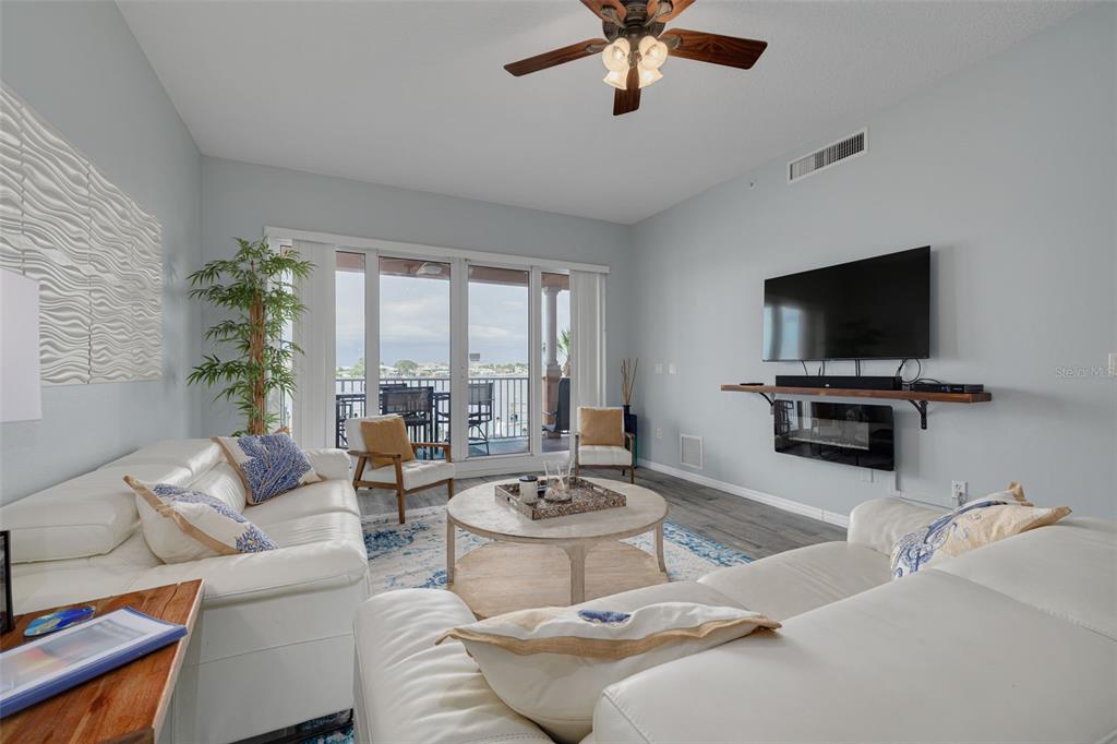 A living room features white sofas, a round coffee table, a wall-mounted television, and balcony access — 530 S GULFVIEW BOULEVARD UNIT 205, CLEARWATER, FL