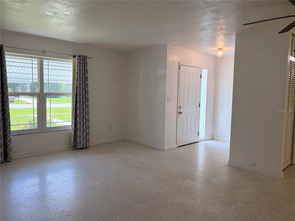 An empty living room with white walls, a front door, and light-colored terrazzo flooring — 1320 HARTLEY AVENUE, DELTONA, FL