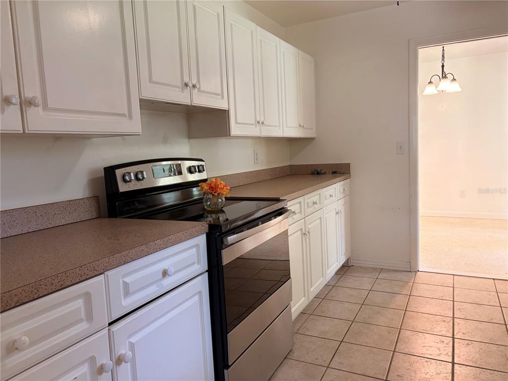A kitchen features white cabinets, a stainless steel stove, and tan countertops over tiled floors — 1320 HARTLEY AVENUE, DELTONA, FL