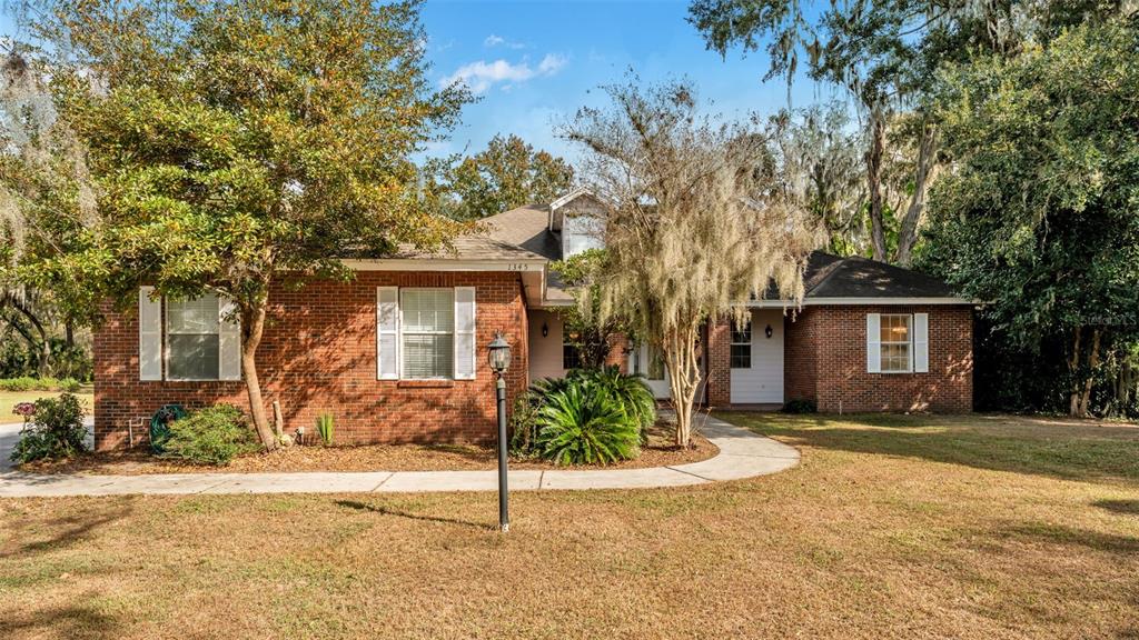 A single-story brick house with white shutters and a curved walkway sits among trees — 1345 LONGOAK DR DRIVE N, LAKELAND, FL