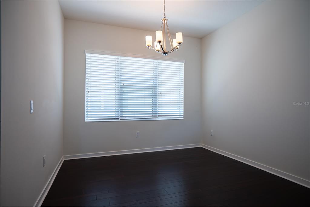 An empty room features dark hardwood floors, white walls, a window with blinds, and a chandelier — 339 8TH STREET N, ST PETERSBURG, FL