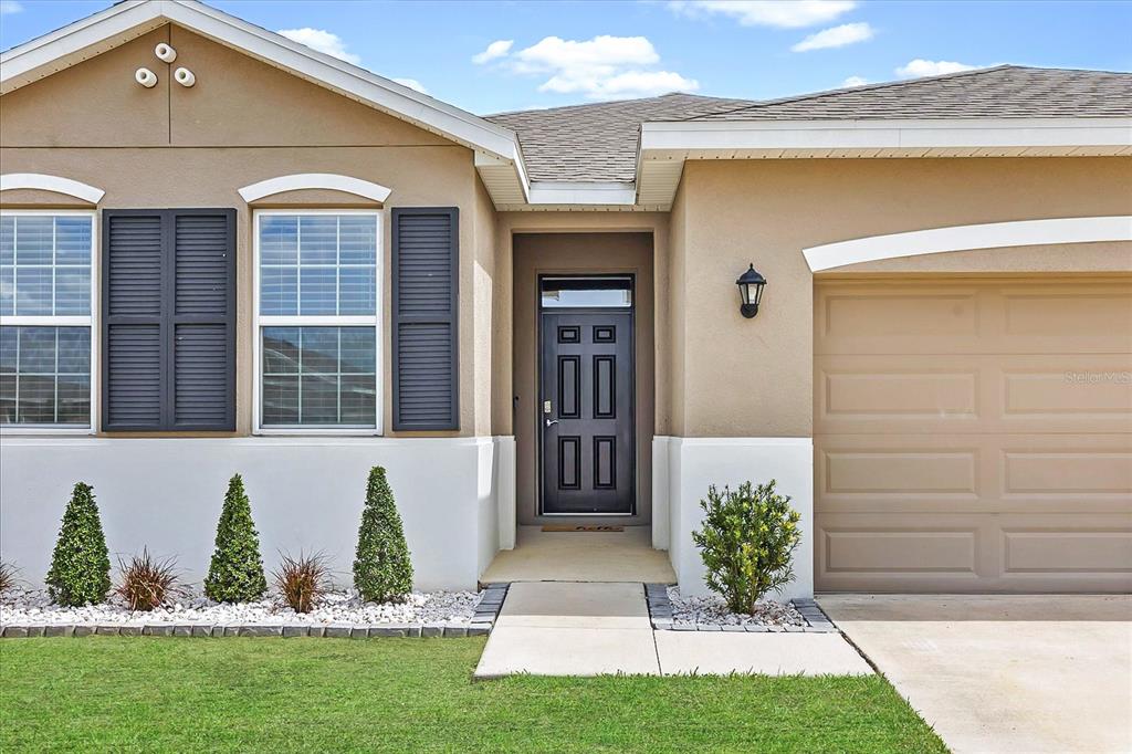 The exterior of a single-story house features a tan facade, dark shutters, and a front door — 8324 WHEAT STONE DRIVE, ZEPHYRHILLS, FL
