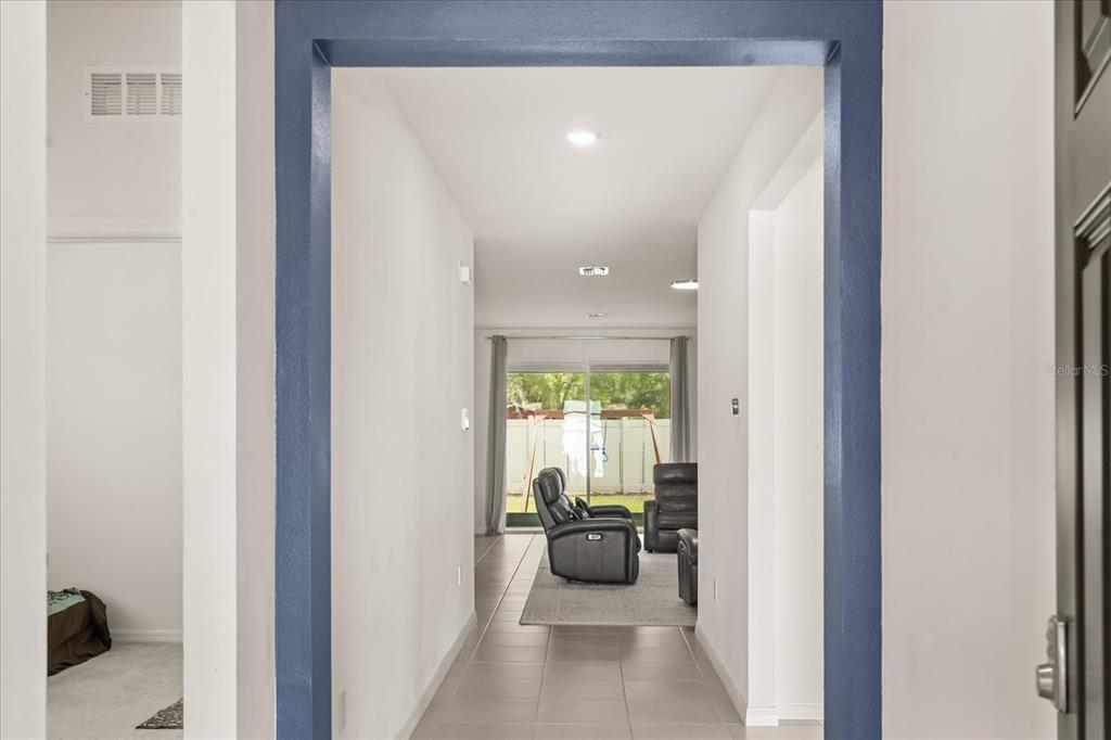 A view through a blue-trimmed doorway into a tiled hallway leading to a living area — 8324 WHEAT STONE DRIVE, ZEPHYRHILLS, FL