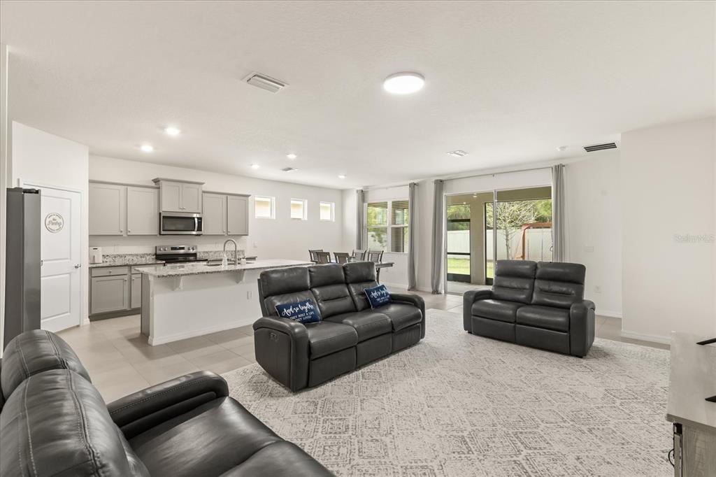 A spacious open-concept living room and kitchen featuring gray cabinetry, granite countertops, and leather furniture — 8324 WHEAT STONE DRIVE, ZEPHYRHILLS, FL