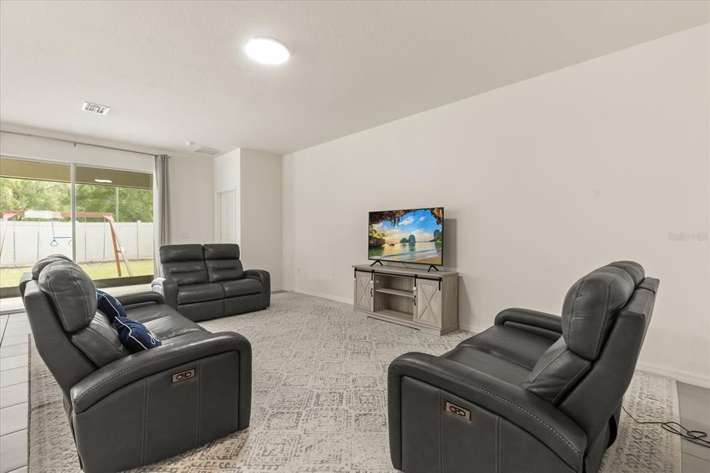 A living room features grey leather reclining sofas, a television on a console, and tile flooring — 8324 WHEAT STONE DRIVE, ZEPHYRHILLS, FL