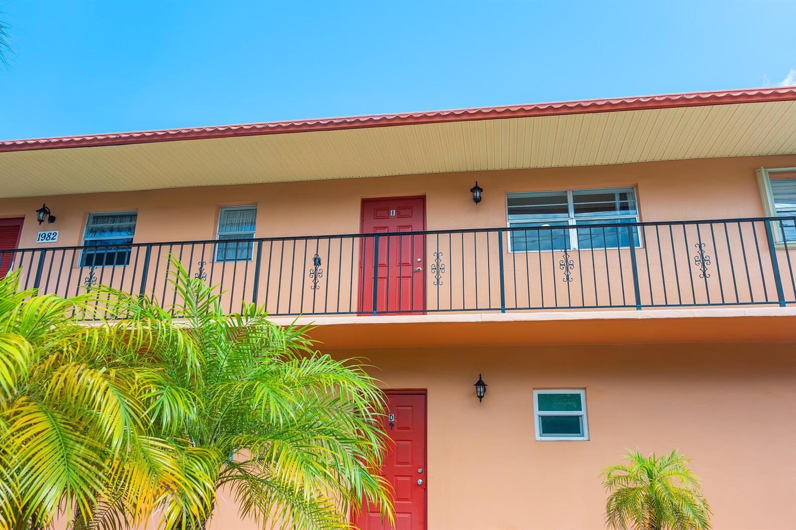 A two-story peach-colored apartment building with red doors and a black metal balcony railing — 1982 SW Palm City Road # I, Stuart FL 34994, STUART, FL