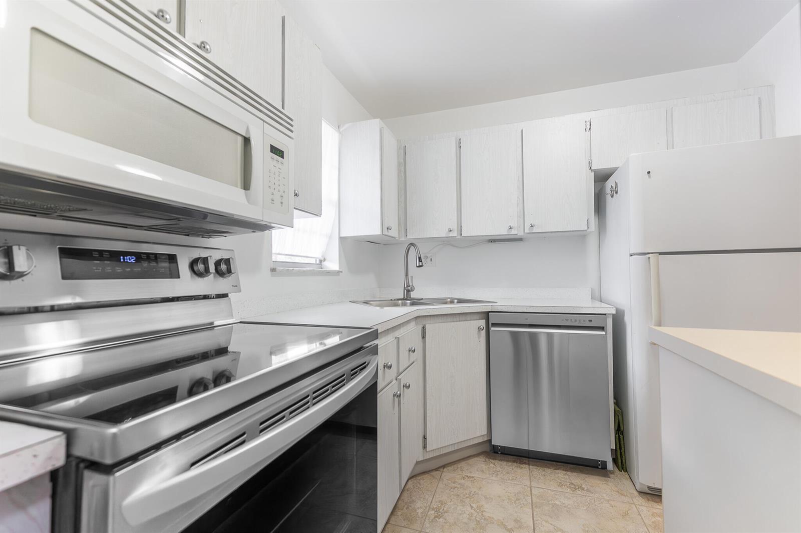 A kitchen features white cabinets, stainless steel appliances, and light-colored tile flooring — 1982 SW Palm City Road # I, Stuart FL 34994, STUART, FL