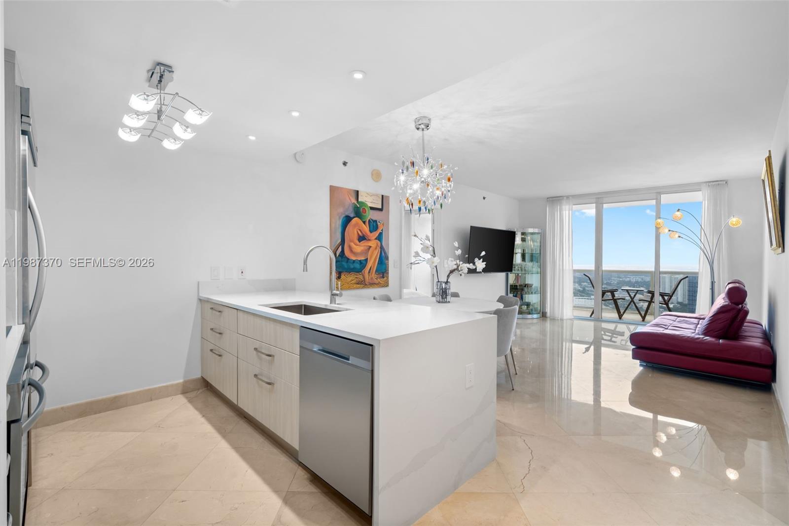 A modern kitchen with light wood cabinets and white countertops opens into a living area — 1850 S Ocean Dr # 4206, Hallandale Beach FL 33009, HALLANDALE BEACH, FL