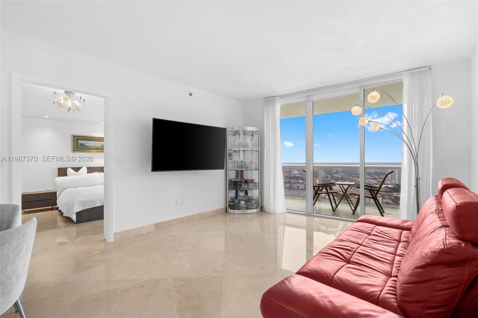 A living room features a red sofa, a wall-mounted television, and a balcony with views — 1850 S Ocean Dr # 4206, Hallandale Beach FL 33009, HALLANDALE BEACH, FL