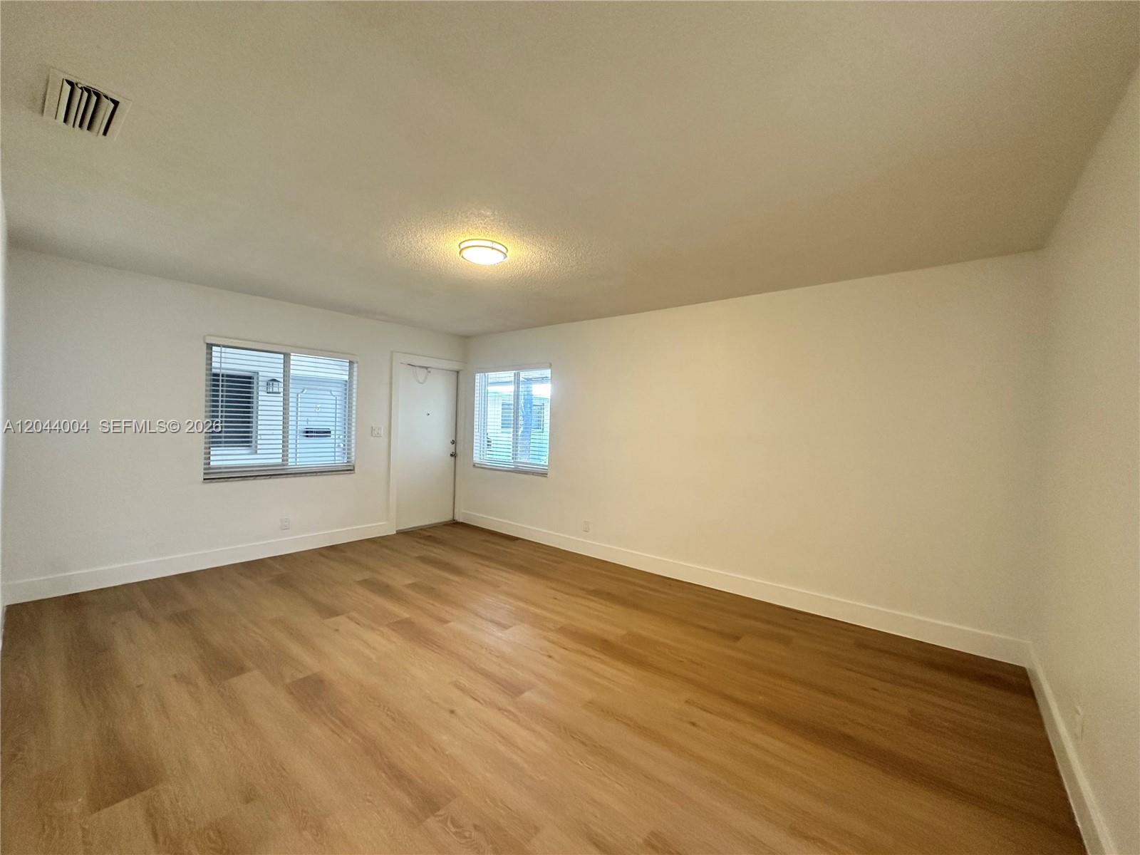An empty room features light wood-look flooring, white walls, two windows, and a door — 3700 NE 22nd Ave # 4, Lighthouse Point FL 33064, LIGHTHOUSE POINT, FL