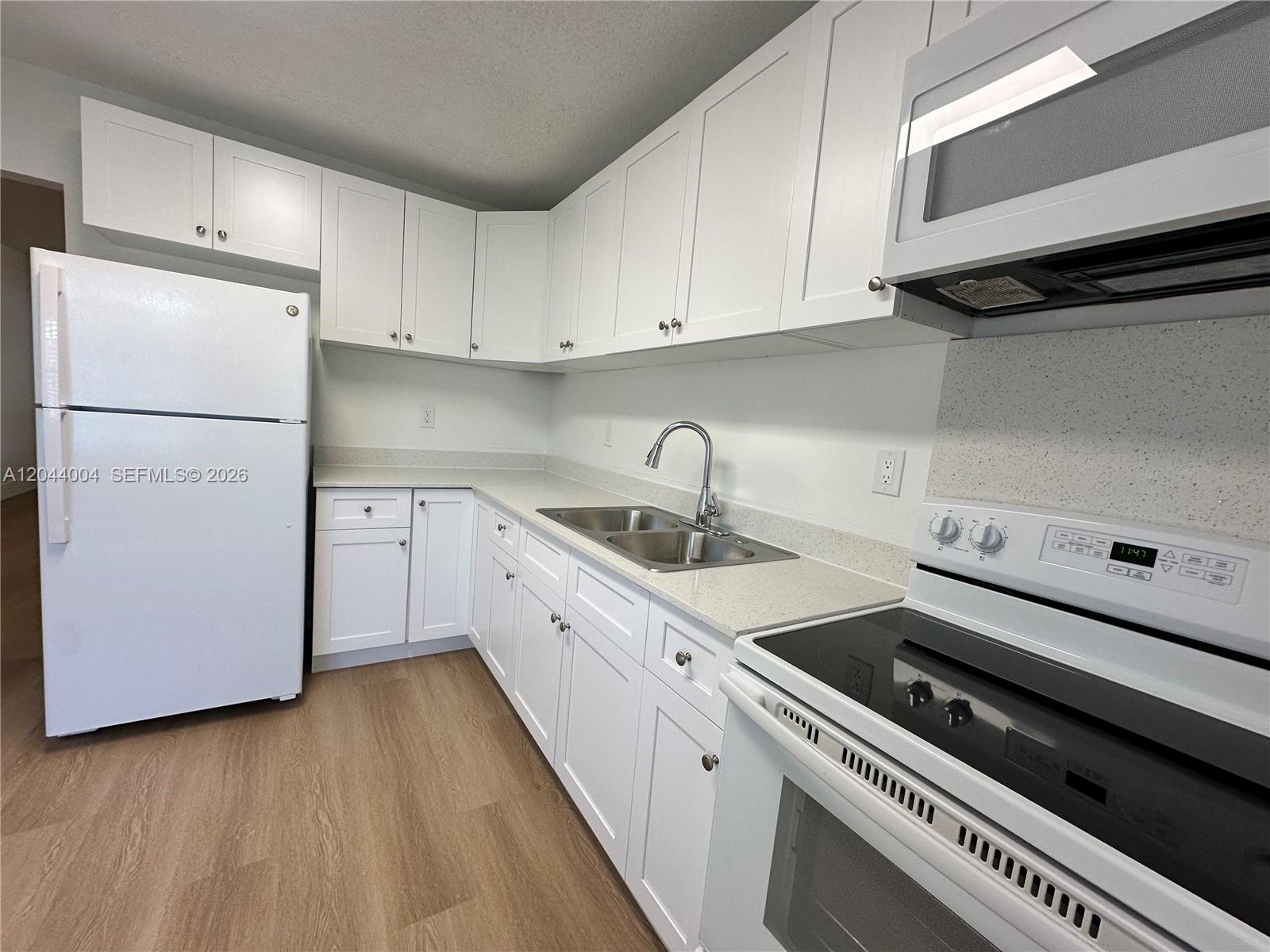 A kitchen features white cabinets, white appliances, light countertops, and wood-look flooring — 3700 NE 22nd Ave # 4, Lighthouse Point FL 33064, LIGHTHOUSE POINT, FL