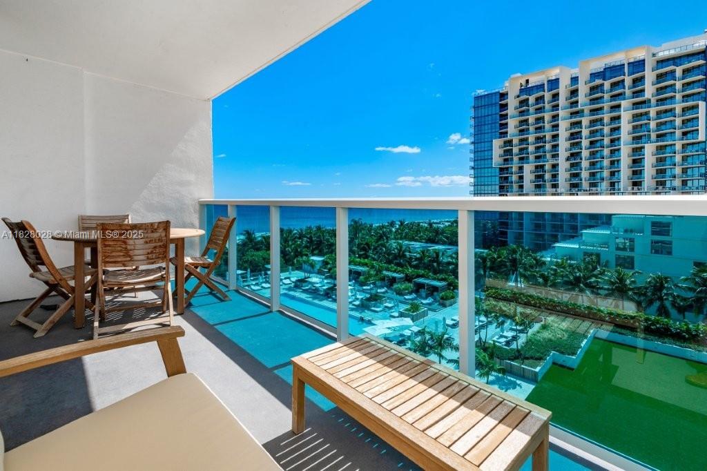 A balcony features wooden furniture overlooking a swimming pool and the ocean — 2301 Collins Ave # 705, Miami Beach FL 33139, MIAMI BEACH, FL