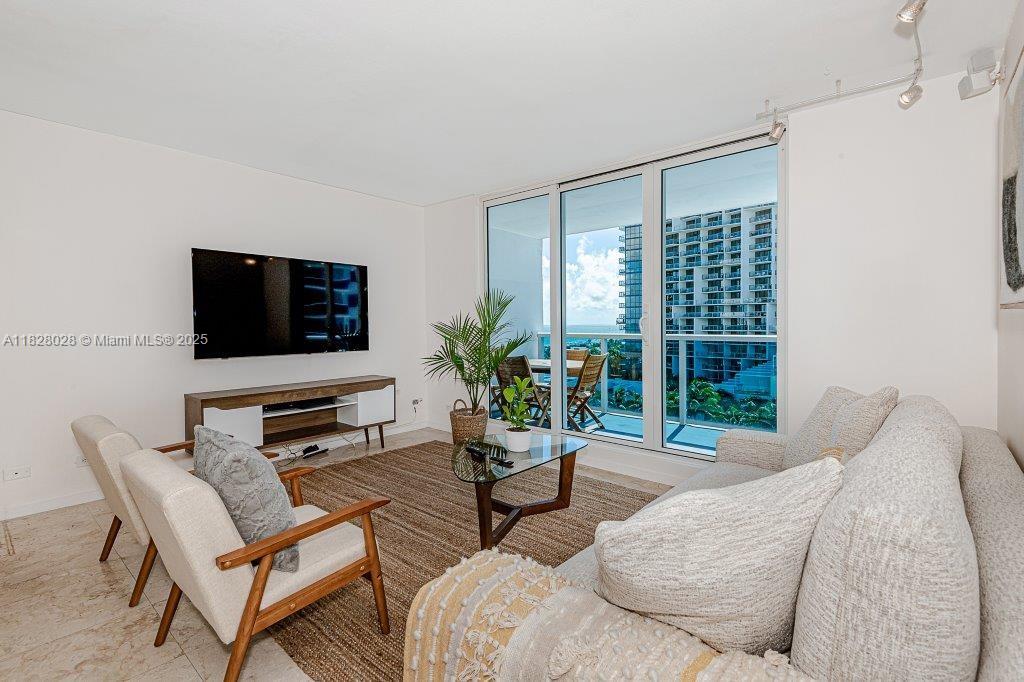 A living room features a television, a sofa, two chairs, and a balcony with ocean views — 2301 Collins Ave # 705, Miami Beach FL 33139, MIAMI BEACH, FL