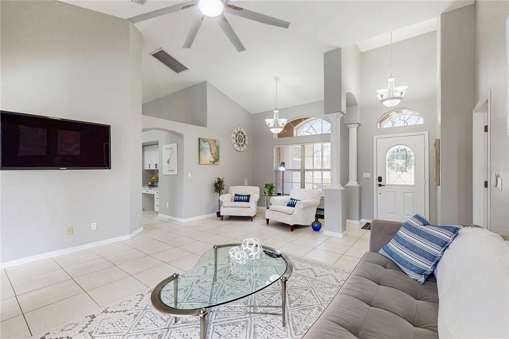 A bright living room features a vaulted ceiling, tile flooring, white armchairs, and a glass-topped table — 1736 NATRONA DRIVE, NORTH PORT, FL