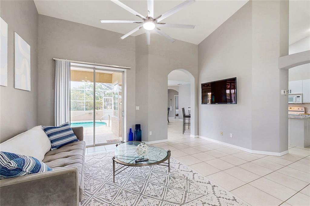 A living room with a vaulted ceiling, tile floors, a ceiling fan, and a sliding door — 1736 NATRONA DRIVE, NORTH PORT, FL