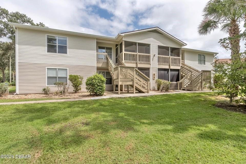 A two-story apartment building features beige siding, screened-in balconies, and wooden exterior staircases — 1600 BIG TREE ROAD UNIT B7, SOUTH DAYTONA, FL