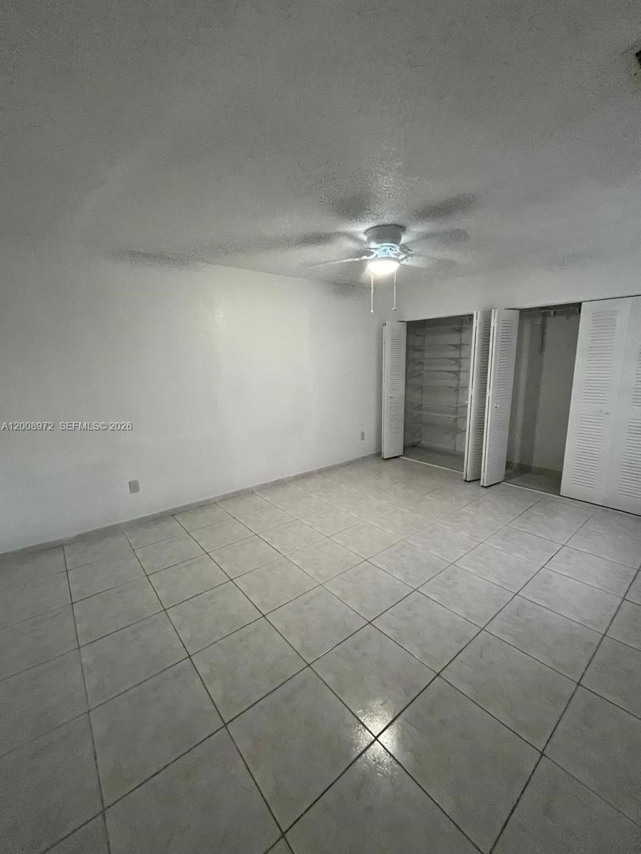 An empty bedroom features white walls, light-colored tile flooring, and a ceiling fan — 9704 NW 6th Ter # 9704, Miami FL 33172, MIAMI, FL