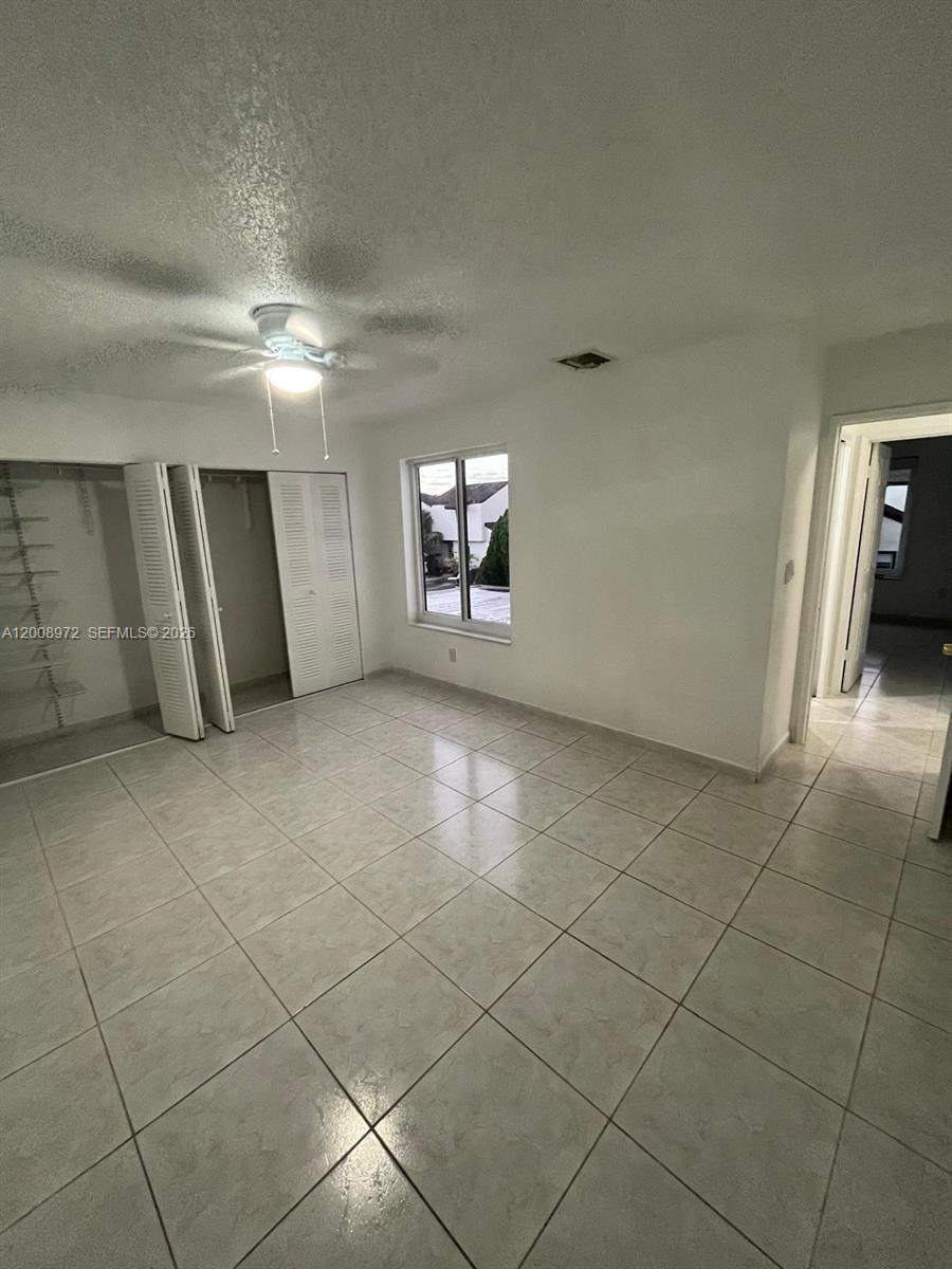 A bedroom with white walls, tile flooring, a ceiling fan, and louvered closet doors — 9704 NW 6th Ter # 9704, Miami FL 33172, MIAMI, FL
