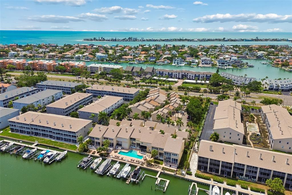 An aerial view shows waterfront apartment buildings with boat slips and a swimming pool — 487 PINELLAS BAYWAY S UNIT 207, ST PETERSBURG, FL