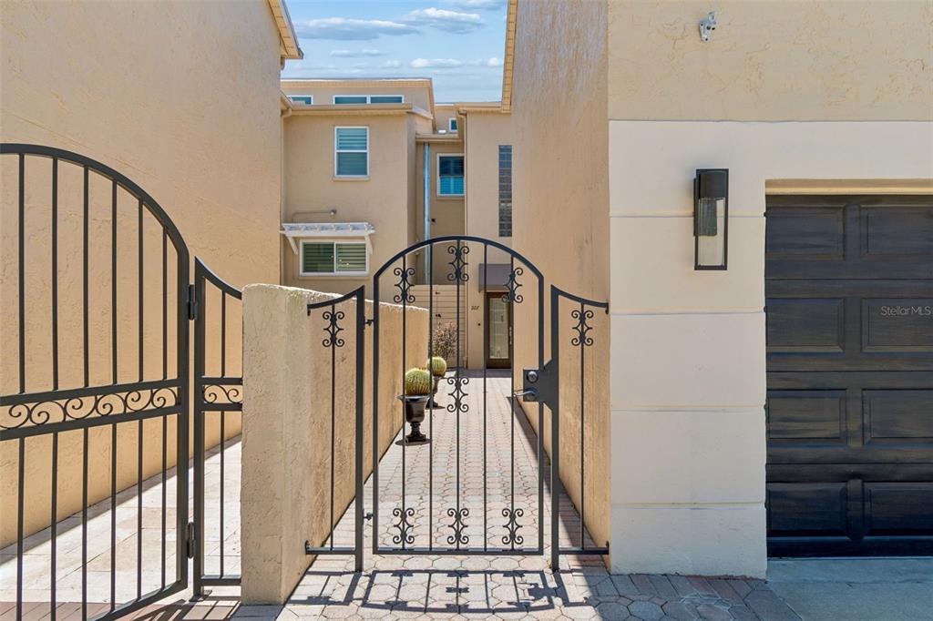 A paved walkway leads through a metal gate to the entrance of a stucco home — 487 PINELLAS BAYWAY S UNIT 207, ST PETERSBURG, FL