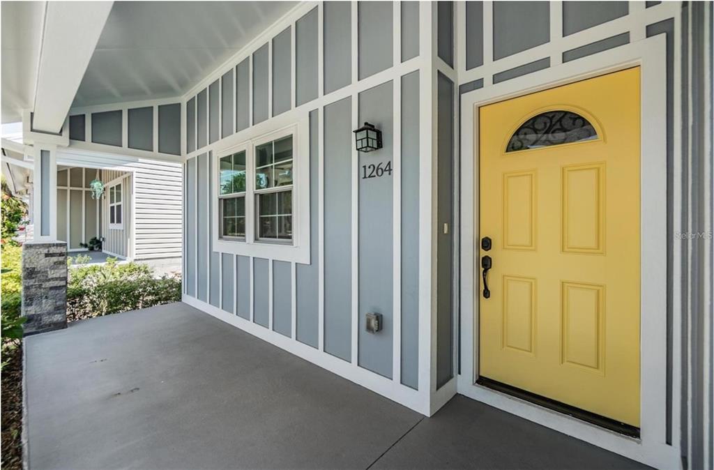 A covered porch features a yellow front door and gray board-and-batten siding — 1264 PIERCE STREET, CLEARWATER, FL