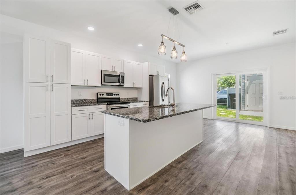 A modern kitchen features white cabinets, granite countertops, a central island, and wood-look flooring — 1264 PIERCE STREET, CLEARWATER, FL