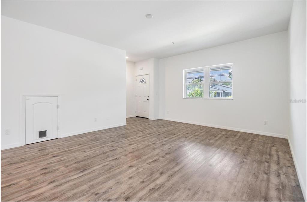 An empty room with white walls, wood-look flooring, a window, and a small pet door — 1264 PIERCE STREET, CLEARWATER, FL