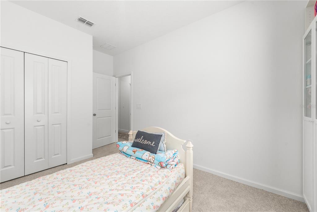 A white kitchen features a central island with three chairs and a dining area nearby — 13941 NW CONVERGENCE BOULEVARD, ALACHUA, FL