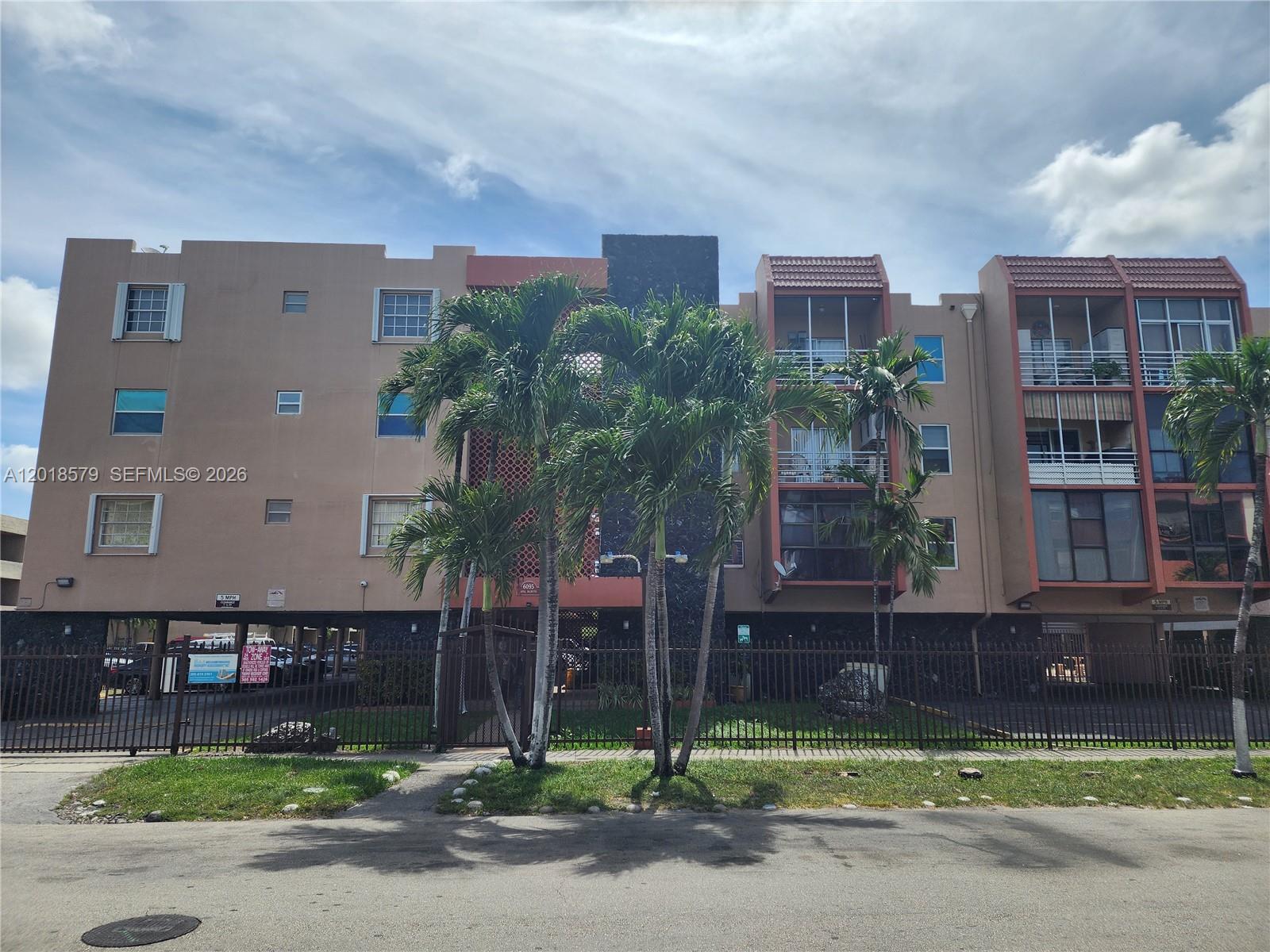 A multi-story apartment building with a gated parking level and palm trees in front — 6095 W 19th Ave # 205, Hialeah FL 33012, HIALEAH, FL
