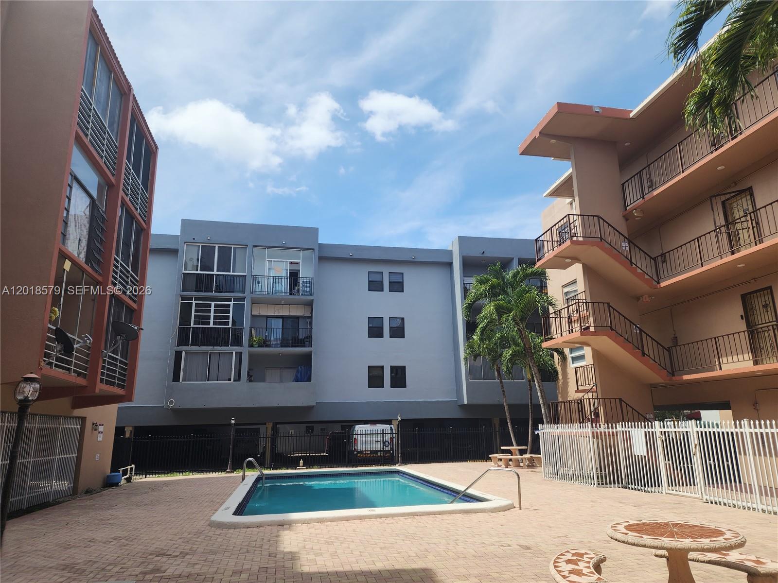 A swimming pool sits in the courtyard between two multi-story apartment buildings — 6095 W 19th Ave # 205, Hialeah FL 33012, HIALEAH, FL