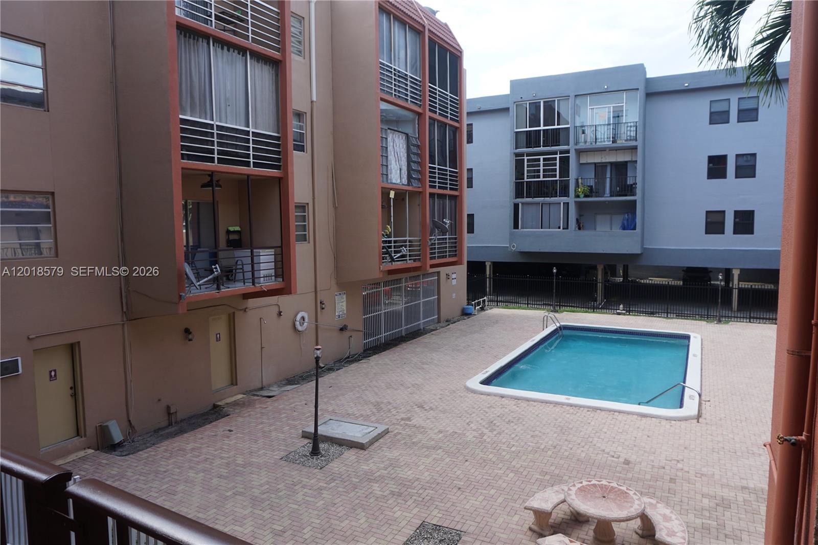 An outdoor swimming pool is situated in a paved courtyard between two apartment buildings — 6095 W 19th Ave # 205, Hialeah FL 33012, HIALEAH, FL