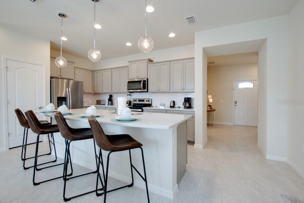 A kitchen features light gray cabinets, a white island with bar stools, and stainless appliances — 8916 SYDNEY AVENUE, KISSIMMEE, FL