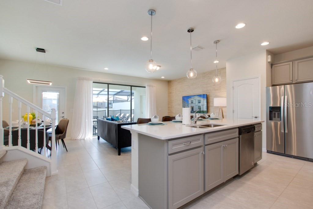 A kitchen with a gray island and stainless steel appliances overlooks a living and dining area — 8916 SYDNEY AVENUE, KISSIMMEE, FL