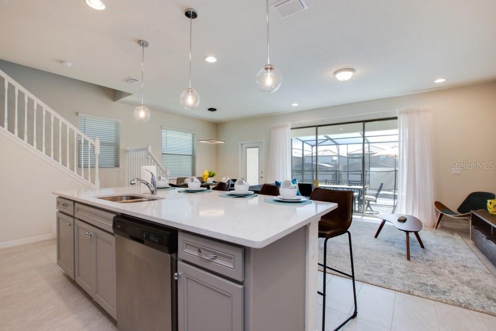 A kitchen island with a stainless steel dishwasher faces a living area with sliding doors — 8916 SYDNEY AVENUE, KISSIMMEE, FL