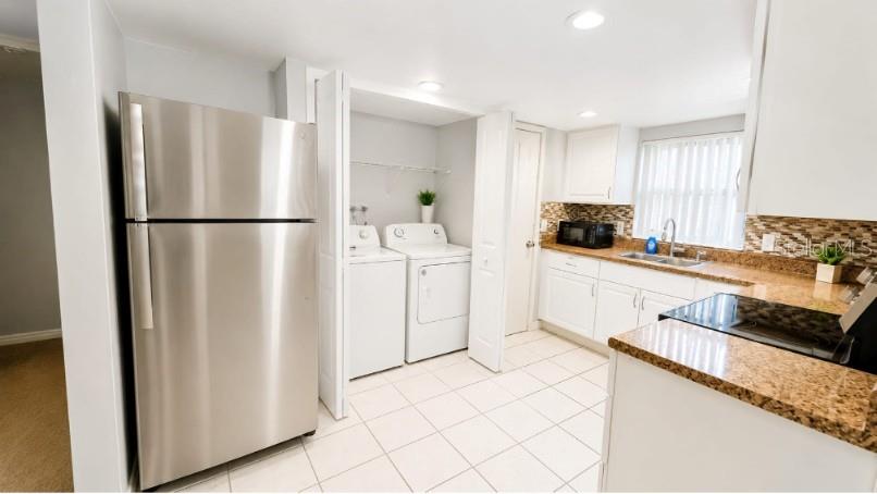 A kitchen features stainless steel appliances, white cabinetry, granite countertops, and an adjacent laundry area — 9919 TURF COURT UNIT 3, ORLANDO, FL