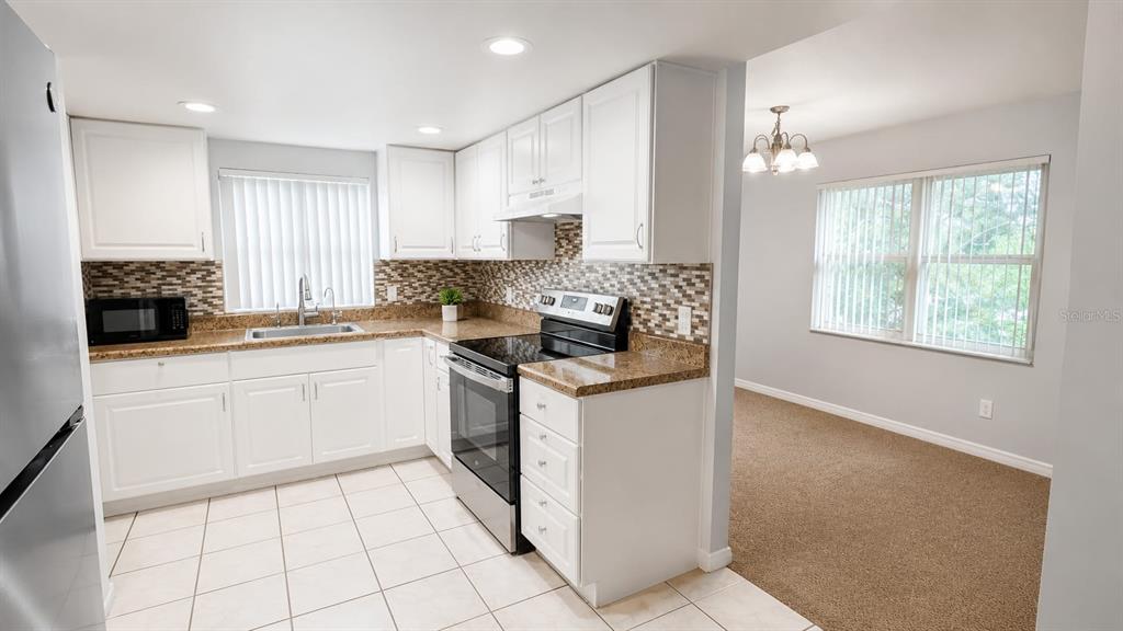 A kitchen with white cabinets, granite countertops, and tile flooring opens to a carpeted dining area — 9919 TURF COURT UNIT 3, ORLANDO, FL