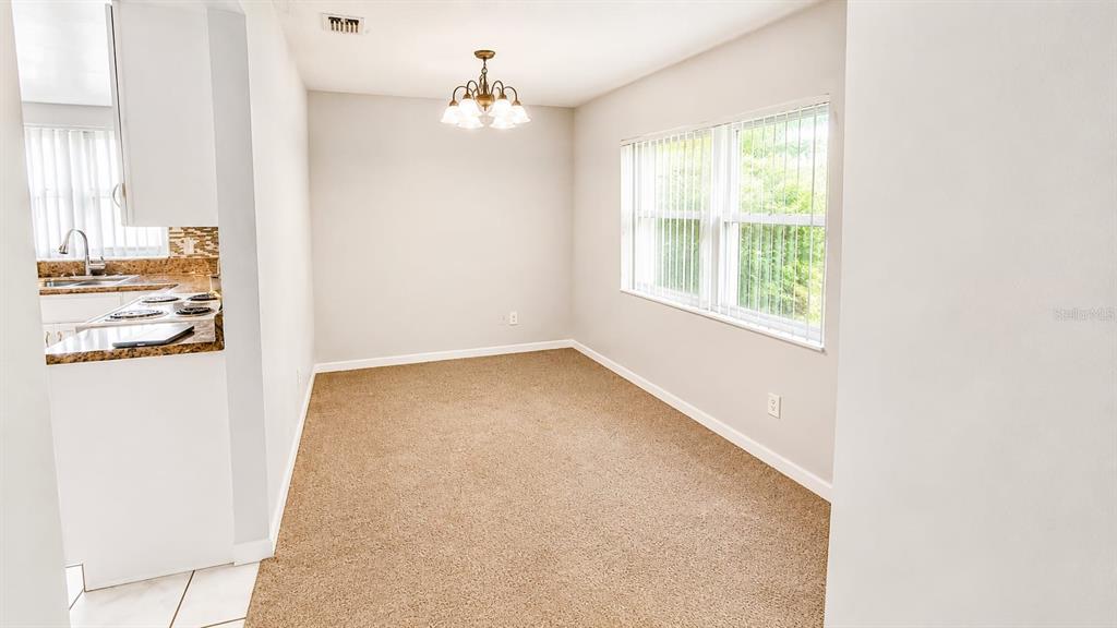A dining area with beige carpet, a chandelier, and a view into the adjacent kitchen — 9919 TURF COURT UNIT 3, ORLANDO, FL