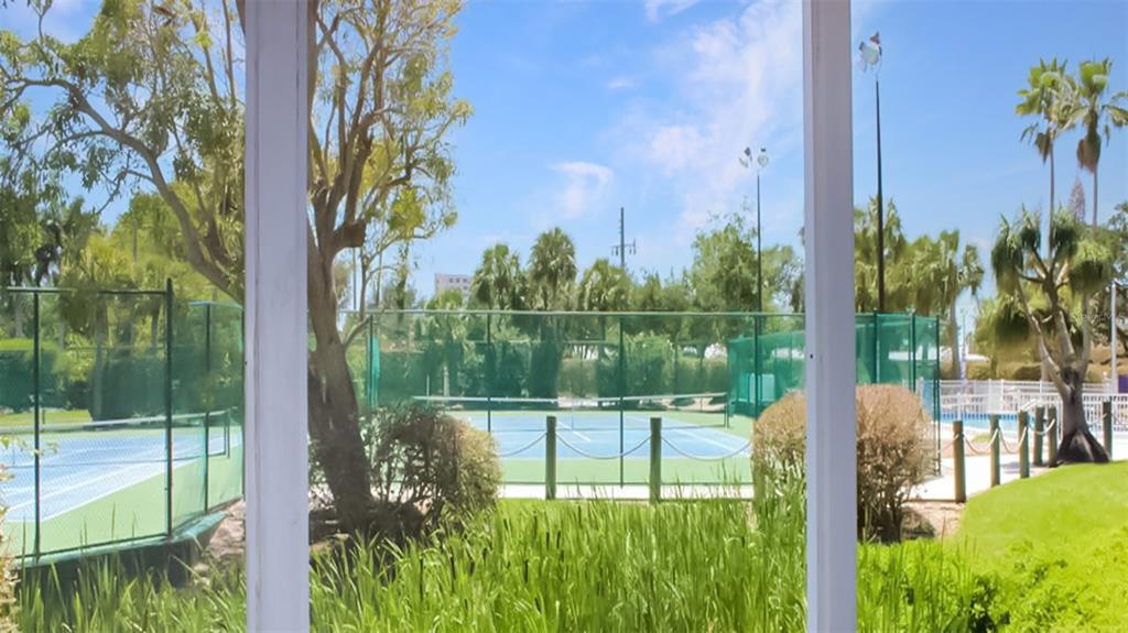 A view through a white frame of a tennis court surrounded by trees and landscaping — 1226 SIESTA BAYSIDE DRIVE UNIT 1226-C, SARASOTA, FL