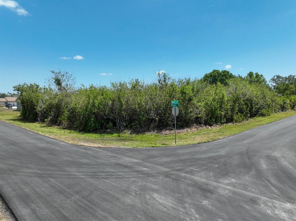 A vacant, overgrown corner lot sits at the intersection of two paved residential streets — 12204 KIRK AVENUE, PORT CHARLOTTE, FL