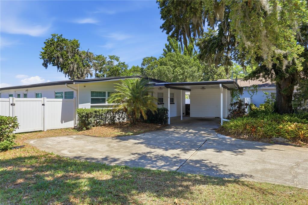 A white single-story house features a carport, a concrete driveway, and a white privacy fence — 5716 MOONLIGHT CIRCLE, ORLANDO, FL