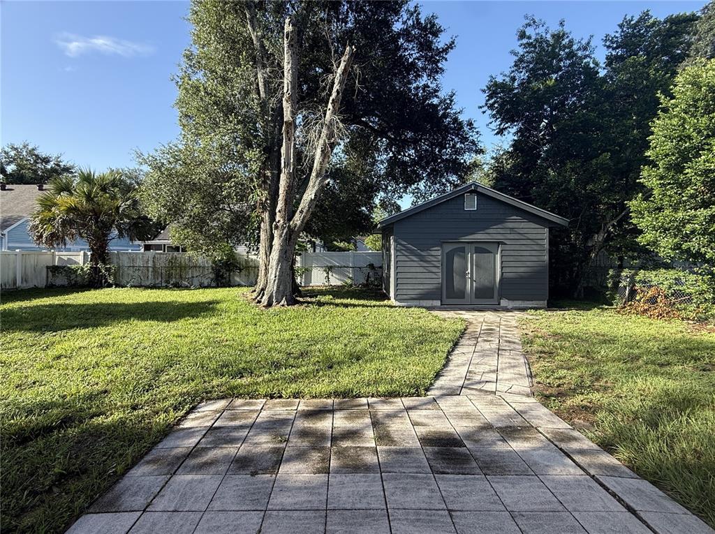 A backyard features a paved walkway leading to a dark gray shed near a tree — 3802 E ESTHER STREET, ORLANDO, FL