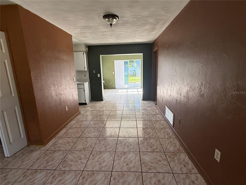 A room with brown walls and light-colored tile flooring leads to a sliding glass door — 3802 E ESTHER STREET, ORLANDO, FL