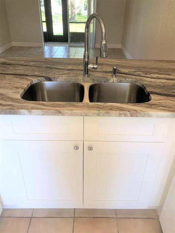 A kitchen sink with a chrome faucet is set into a marble-patterned countertop above white cabinets — 10109 BLAZED TREE COURT, ORLANDO, FL