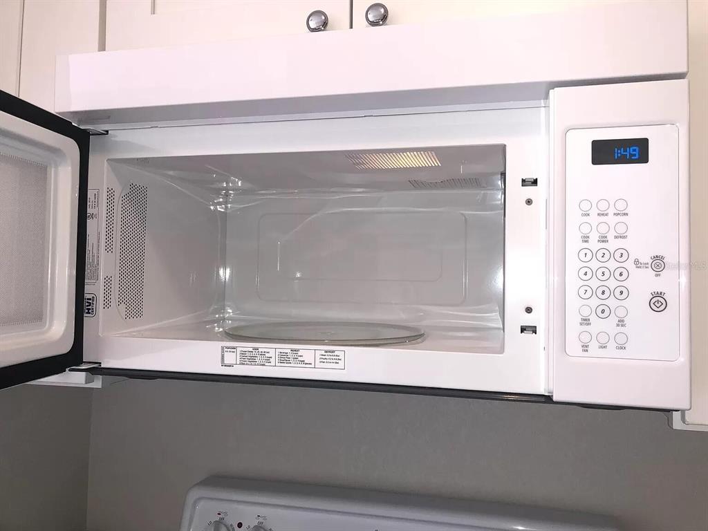 A white over-the-range microwave is mounted above a stove in a kitchen — 10109 BLAZED TREE COURT, ORLANDO, FL