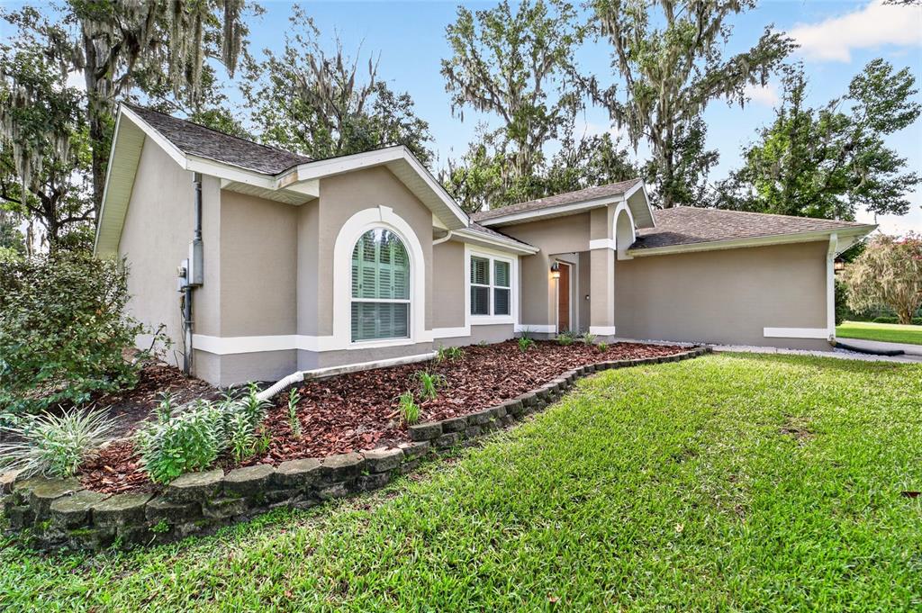 A single-story house with tan stucco walls, a stone retaining wall, and arched windows — 4849 NW 83RD COURT, OCALA, FL