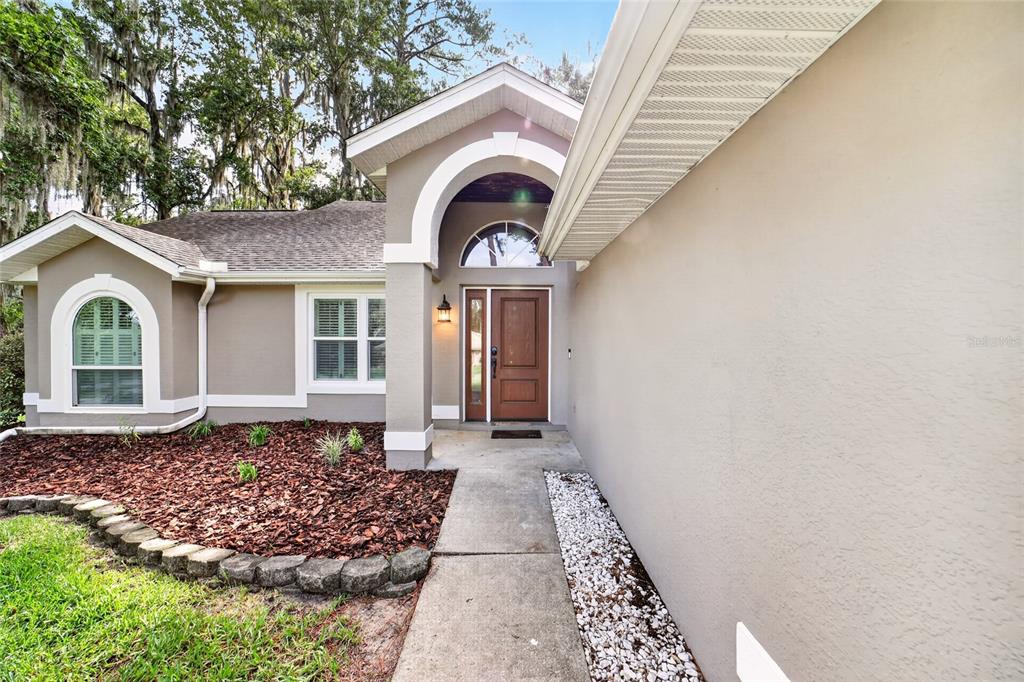 A tan house exterior features a front entrance with an arched doorway and walkway — 4849 NW 83RD COURT, OCALA, FL